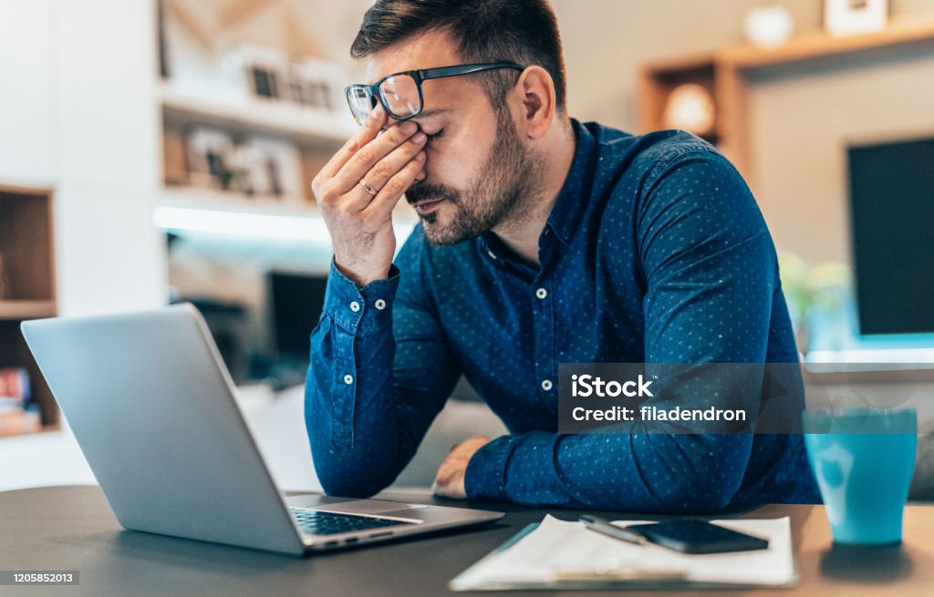 Tired young businessman working at home using lap top and looking Anxious